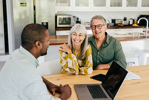 A senior couple sits with a professional, discussing life insurance options. They review documents, focusing on structuring life cover within their financial plan, including ownership, beneficiaries, premiums, and coverage to ensure it meets their long-term needs.